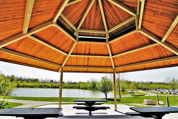 The camera looks out over a pond and parking area from under a covered pavilion with picnic tables.